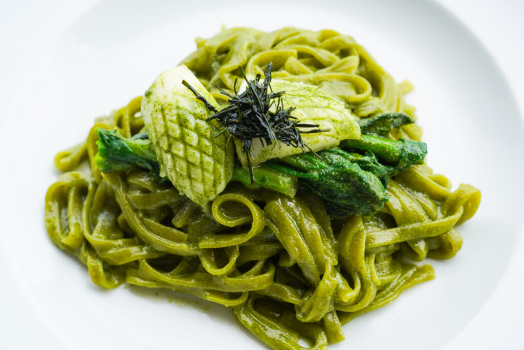 Pasta in a green sauce topped with vegetables, squid, and nori.