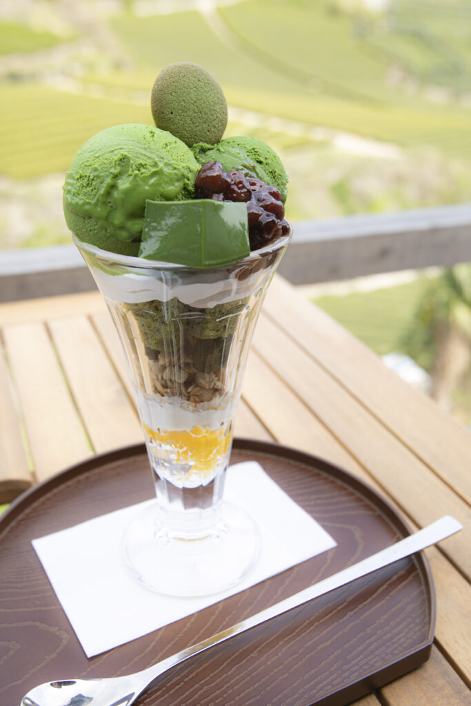 A parfait featuring granola, whipped cream, red bean paste, and matcha-flavored cake, ice cream, and jelly.