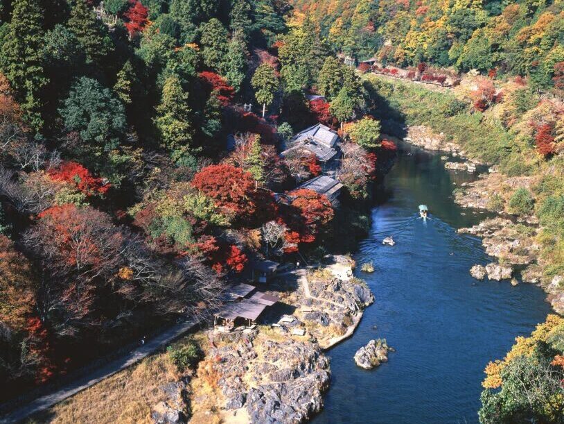 Hozukyo Gorge featuring houses, a boat in the river, and colorful trees