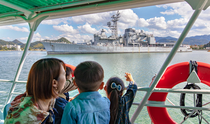 A family on a sightseeing boat in Maizuru bay waving at Japanese naval vessel