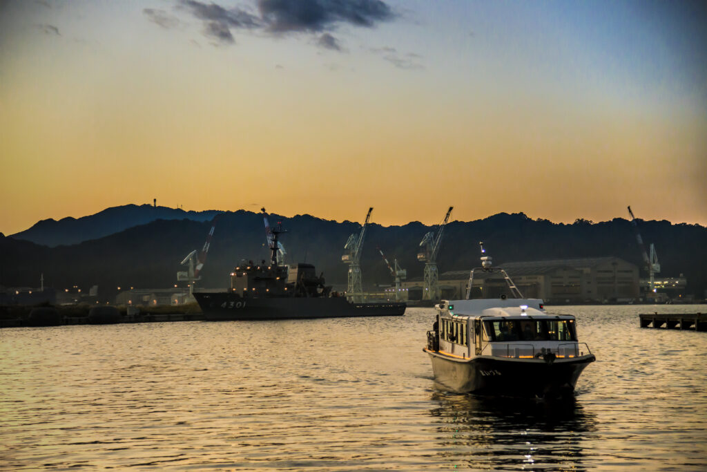 Tour boat in Maizuru bay in the evening with naval vessels in the background